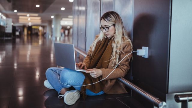 Jovem sentada com um laptop no colo em um local público